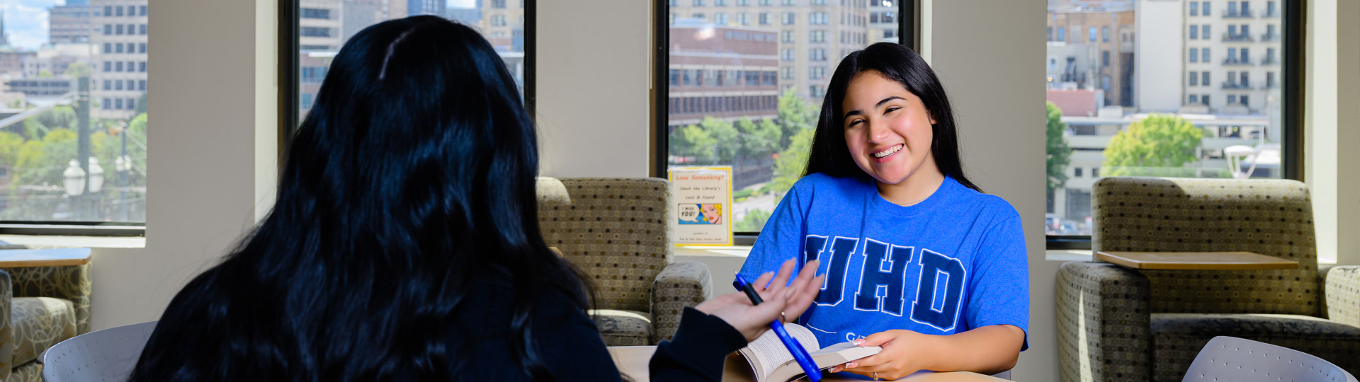 Two UHD students sitting at a table on campus, talking and smiling 