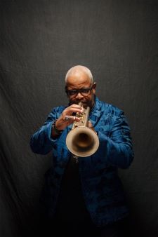 Terence Blanchard portrait. He is playing a trumpet and wearing a blue coat.