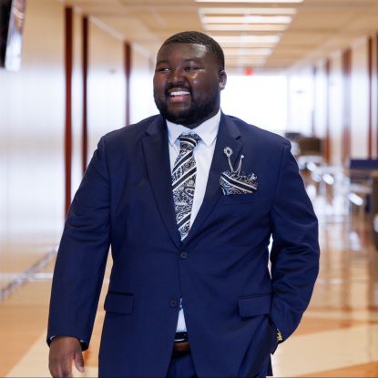 John Stubblefield is a blue suit. He is standing in a hallway.