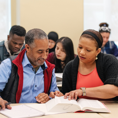 Female instructor looks at a thick book with an older adult student