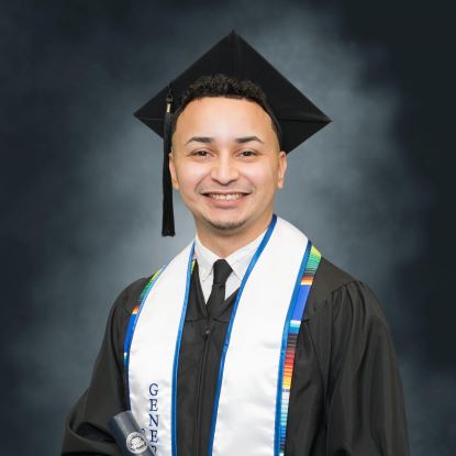 Andy Berrios sits for a photo portrait. He is wearing a graduation cap and gown.