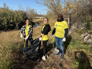 Three students picking up trash. The middle student has a trash bag in hand.