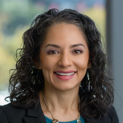 Monica Comeaux's headshot. She is wearing a black jacket and silver necklace with a blue shirt.