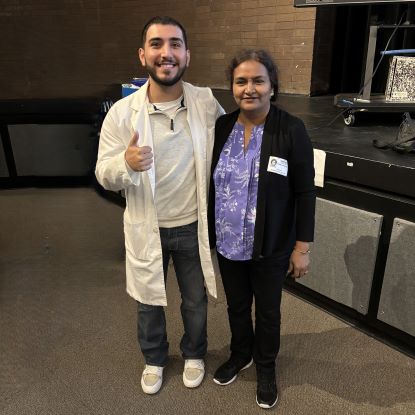 UHD students and faculty pose for a photo. The student is wearing a white lab coat.