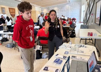 A saint thomas high school student stands with his hands behind his back as a University of Houston-Downtown student in Organic Chemistry explains a service learning project on the effect of drugs on the body.